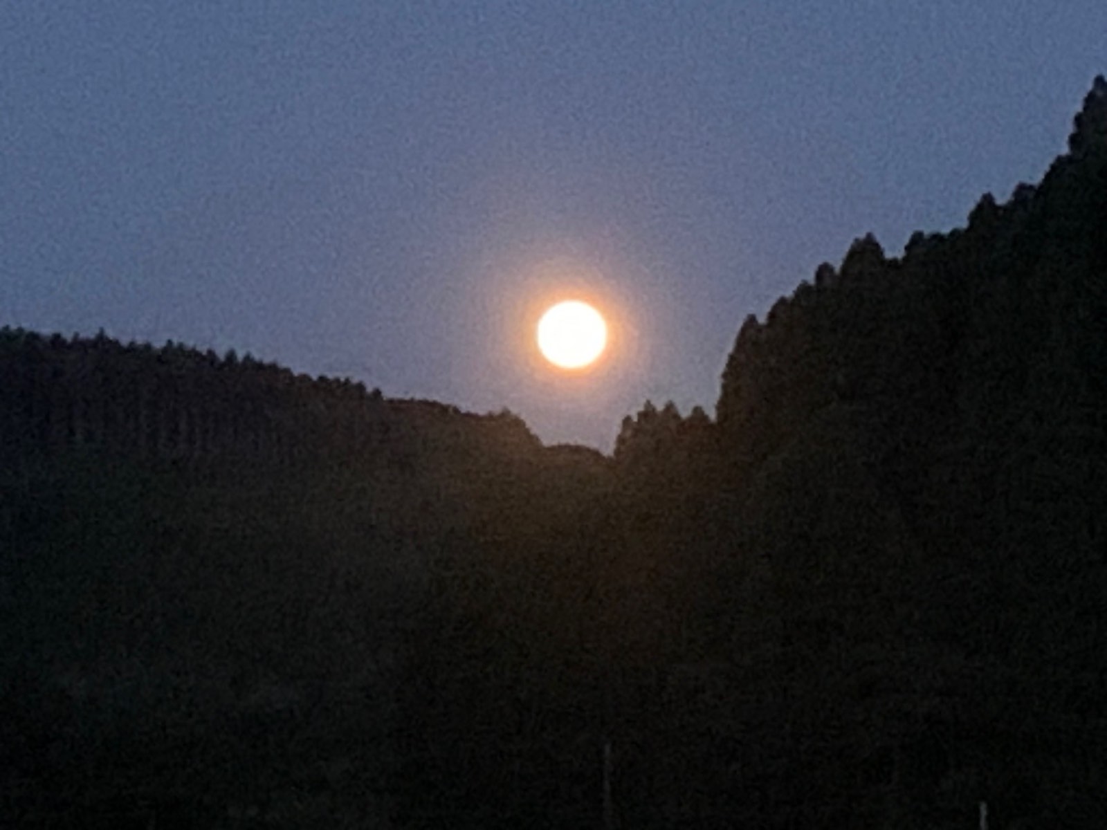 山の稜線から昇るオレンジ色の月
